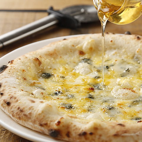 立川駅1分、本格パスタが美味しいイタリアン＆スパニッシュのお店『CANTINA 立川店』でいただける、チーズがたっぷり乗ったピザ(ピッツァ)〈クアトロフォルマッジ〉にハチミツをかけている画像