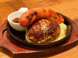 京都駅近くにある肉が旨いカフェ[NICK STOCK イオンモールKYOTO店]にて提供するプレーンハンバーグに極太ソーセージをトッピングした写真